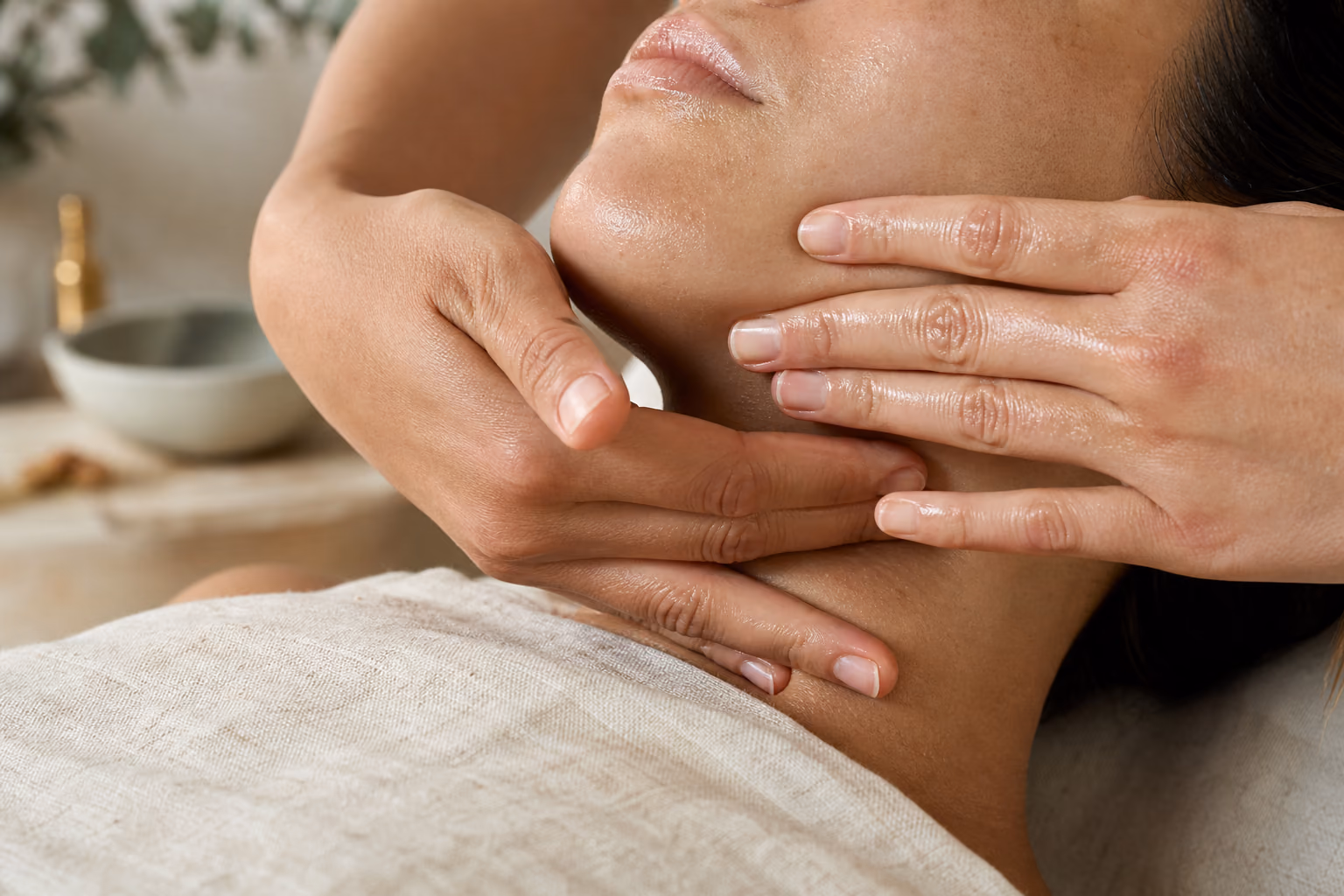 An esthetician's hands massaging along a client's jaw and neck during a Signature Facial.