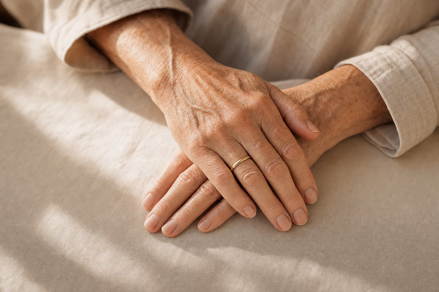 A pair of mature hands resting one over the other on linen.