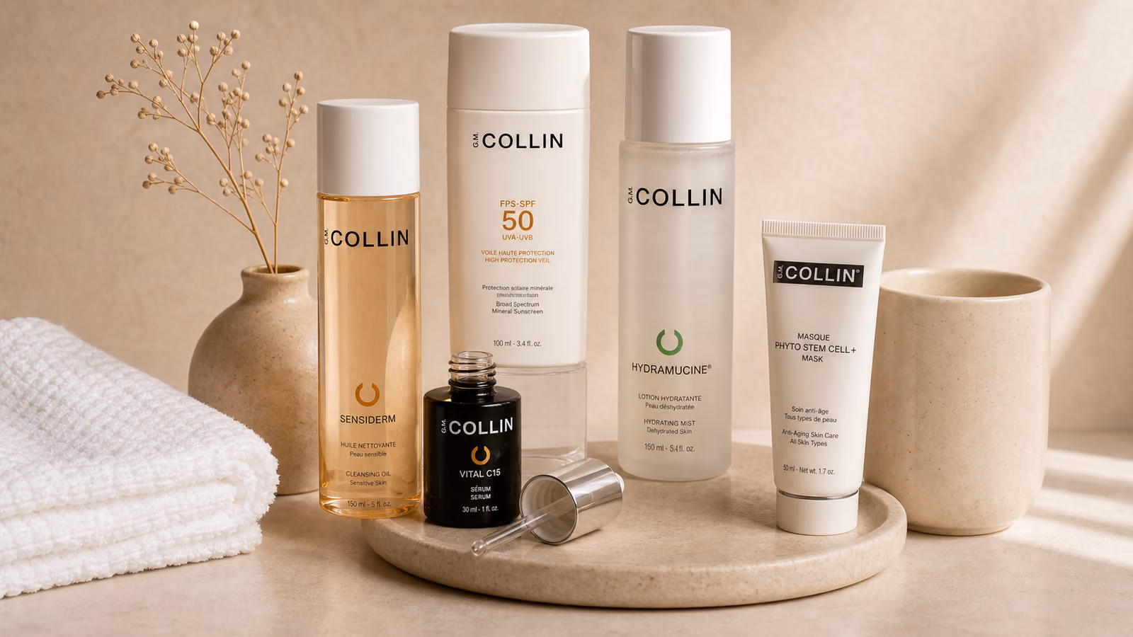 A row of G.M. Collin skincare — cleanser, SPF 50, serum and mask — arranged on a stone tray.